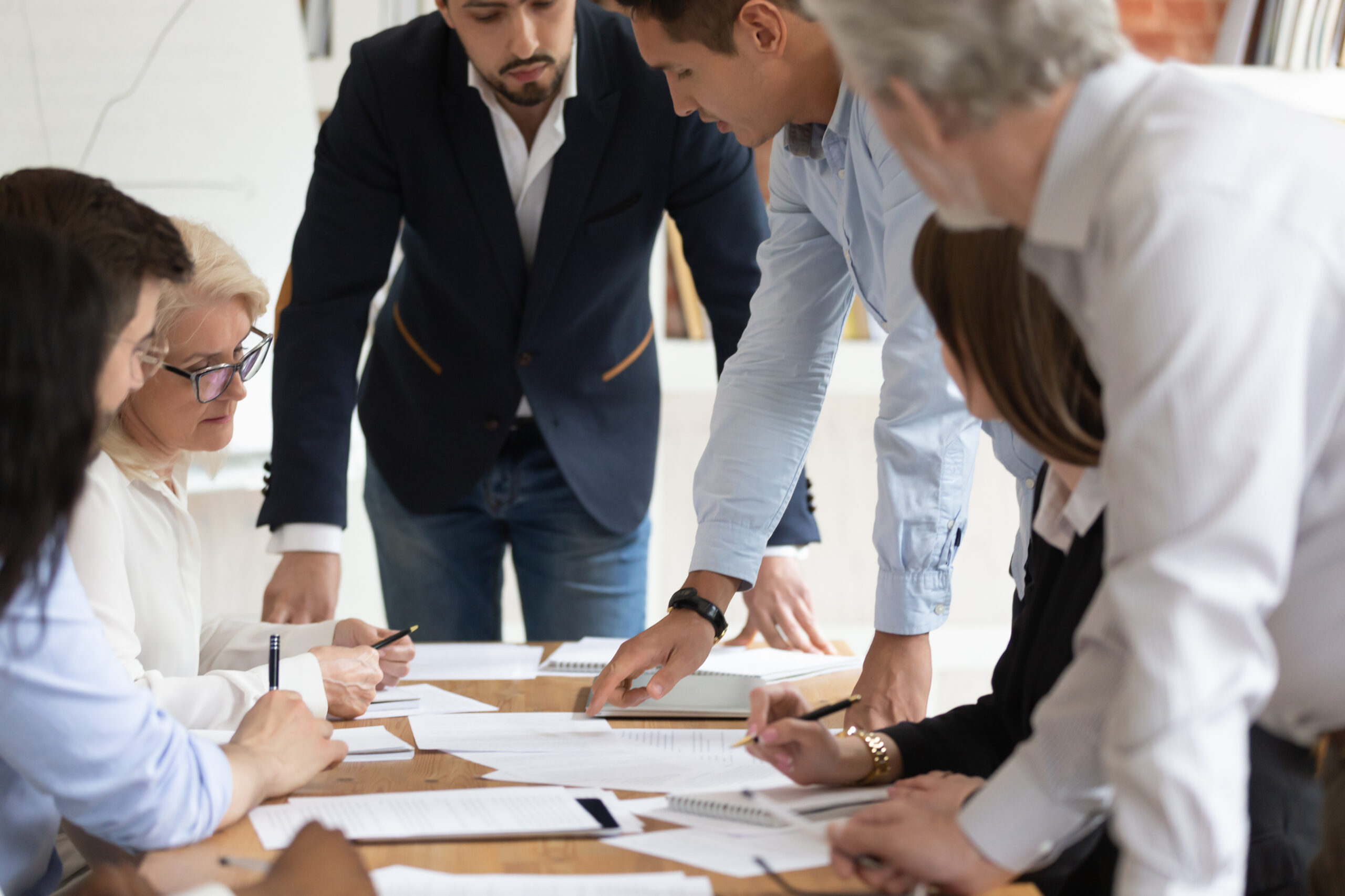 Focused multi-ethnic diverse businesspeople company employees brainstorming during office meeting at boardroom, search problem solution, discuss contract terms and conditions before signing document