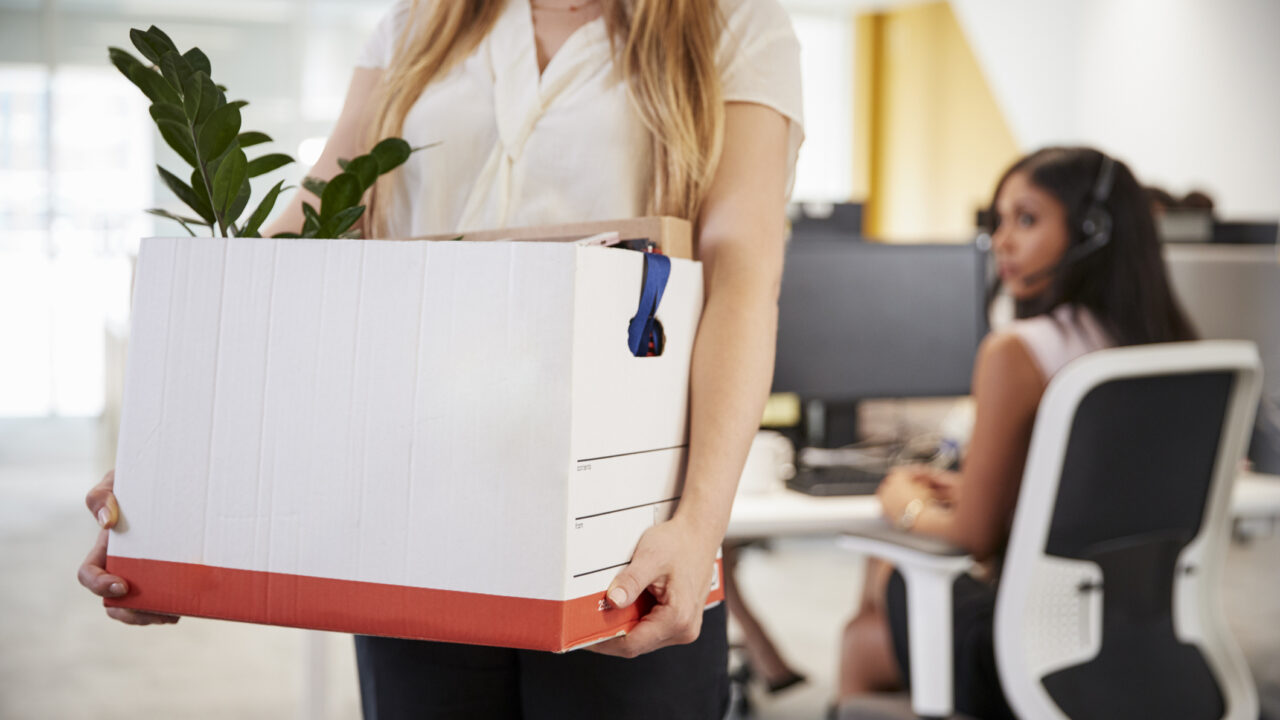 Fired female employee holding box of belongings in an office