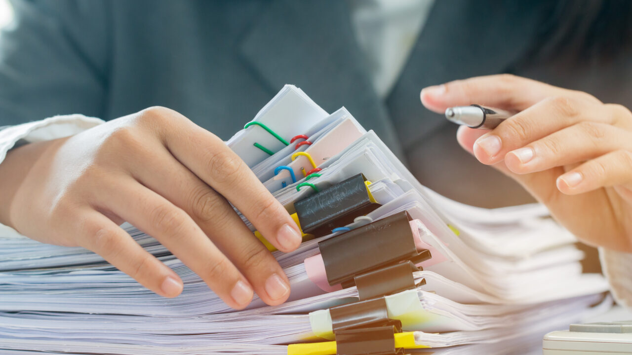 Accounting planning budget concept : Business woman offices working for arranging documents unfinished stack of document papers with pen, calculator, clip papers on busy office desk
