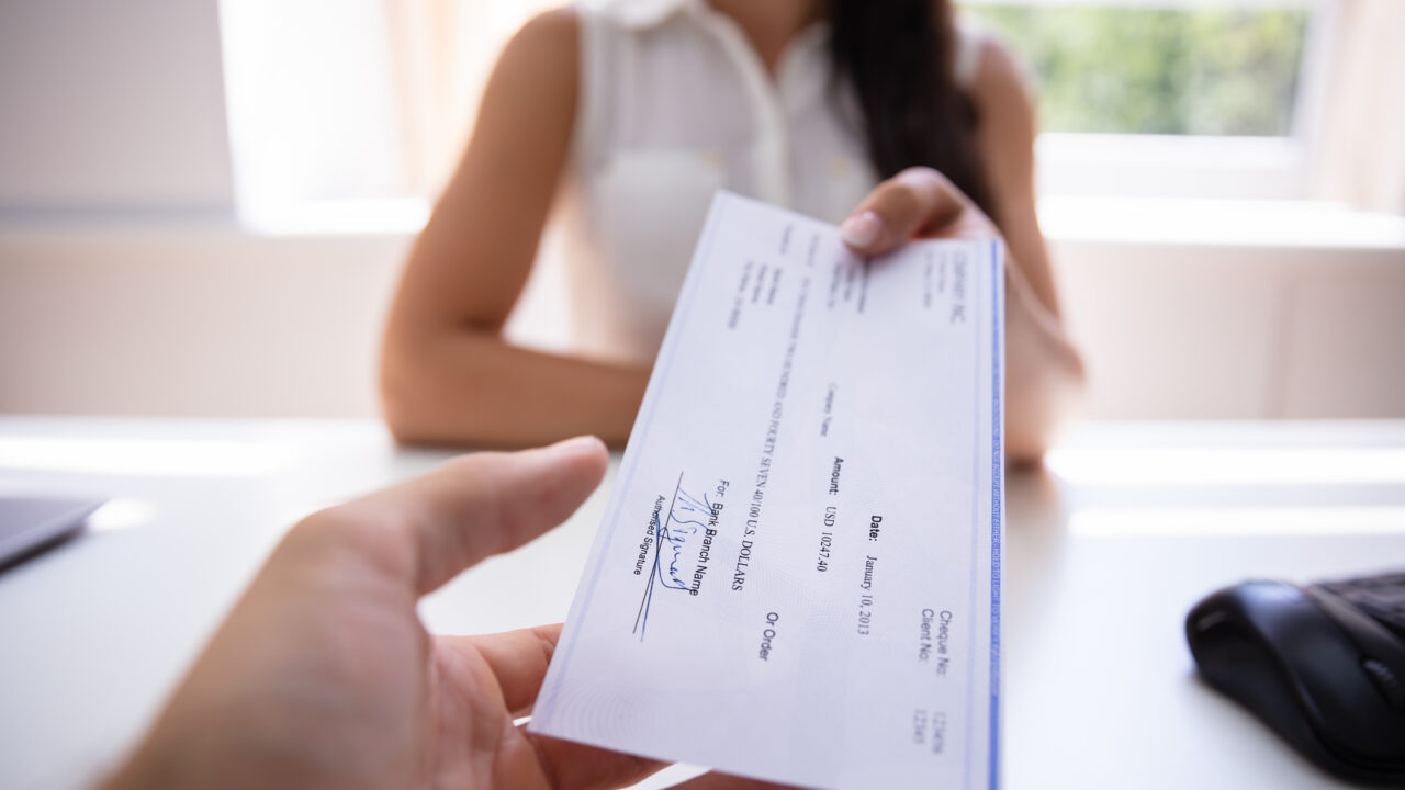 Close-up Of A Businesswoman's Hand Giving Cheque To Colleague