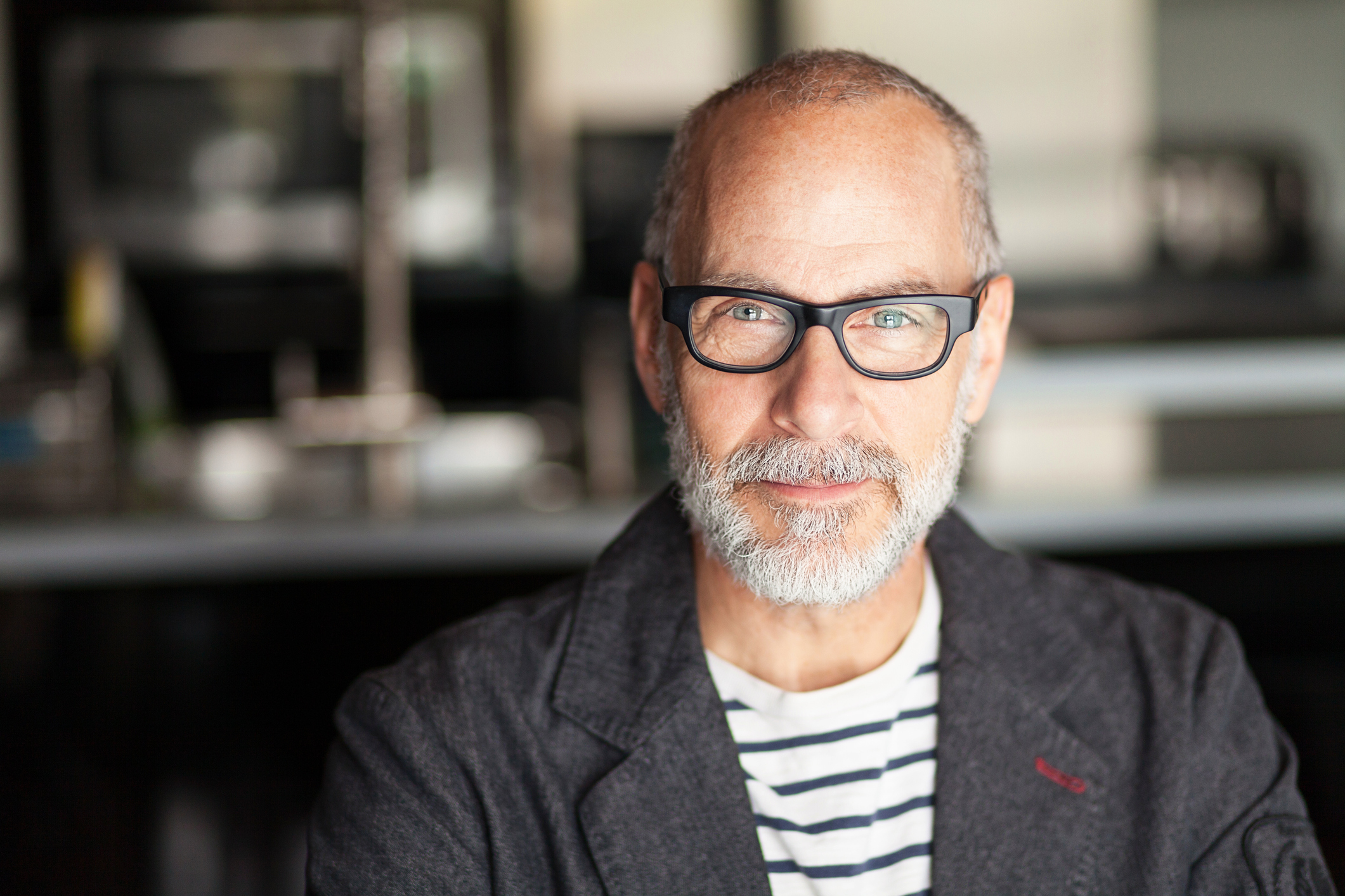 Portrait Of A Senior Man Looking At The Camera. He's confident. He's working at home. Kitchen background. He's wearing eyeglasses